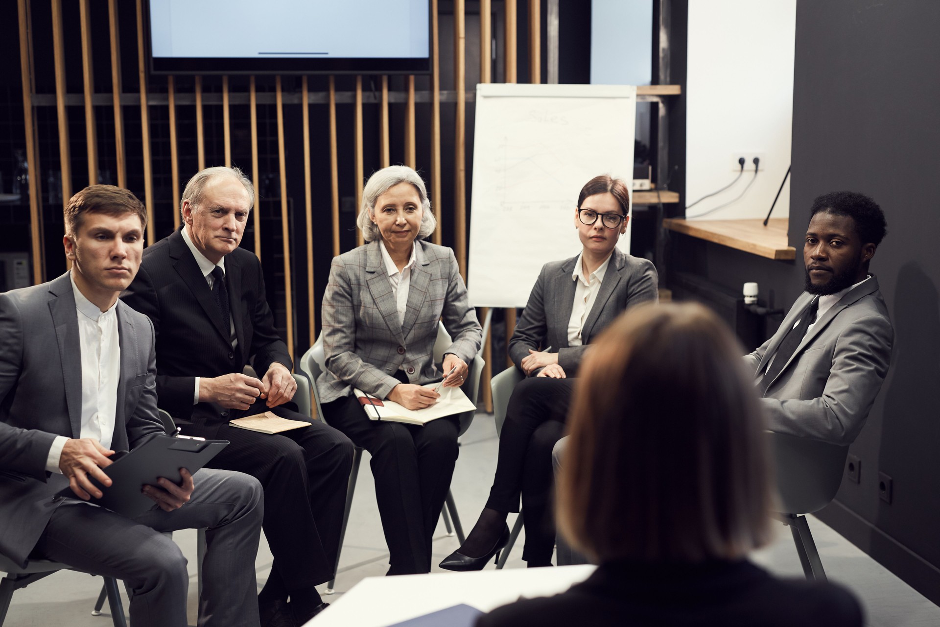 Group of serious multi-ethnic business people of different ages sitting in semi-circle against teacher and listening to her attentively at refresher course